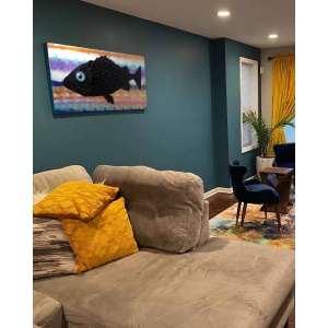 Nekol’s Fish #2 oil painting in a home interior: A single, surreal black fish floats across a vibrant, layered background of abstract, wave-like colors