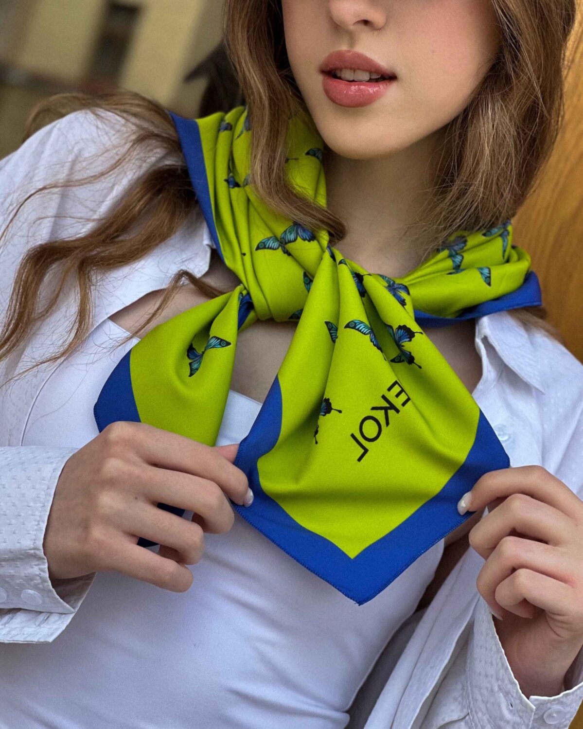 Blue butterfly silk scarf styled around the neck, showcasing lime and azure pattern.
